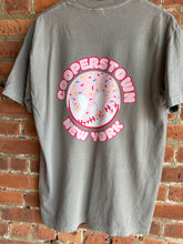 Load image into Gallery viewer, Gray t-shirt with a colorful graphic design on a brick wall background