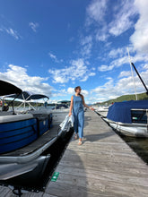 Load image into Gallery viewer, Woman in a blue dress standing on a dock with boats and a clear sky in the background