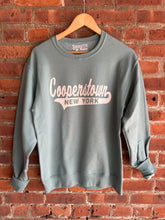 Load image into Gallery viewer, Sage Green sweatshirt with 'Cooperstown New York' text on a wooden hanger against a brick wall.