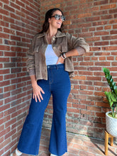 Load image into Gallery viewer, Woman in a brown jacket and blue jeans standing against a brick wall.
