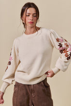 Load image into Gallery viewer, Woman wearing a cream sweater with floral sleeves against a beige background
