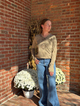 Load image into Gallery viewer, Person standing on a brick sidewalk with flowers and a plant against a brick wall.
