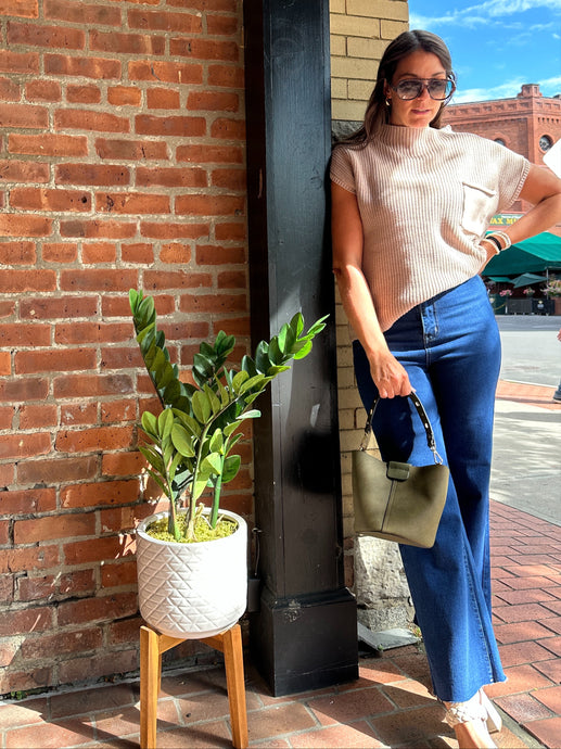 Woman leaning against a brick wall with a plant and handbag